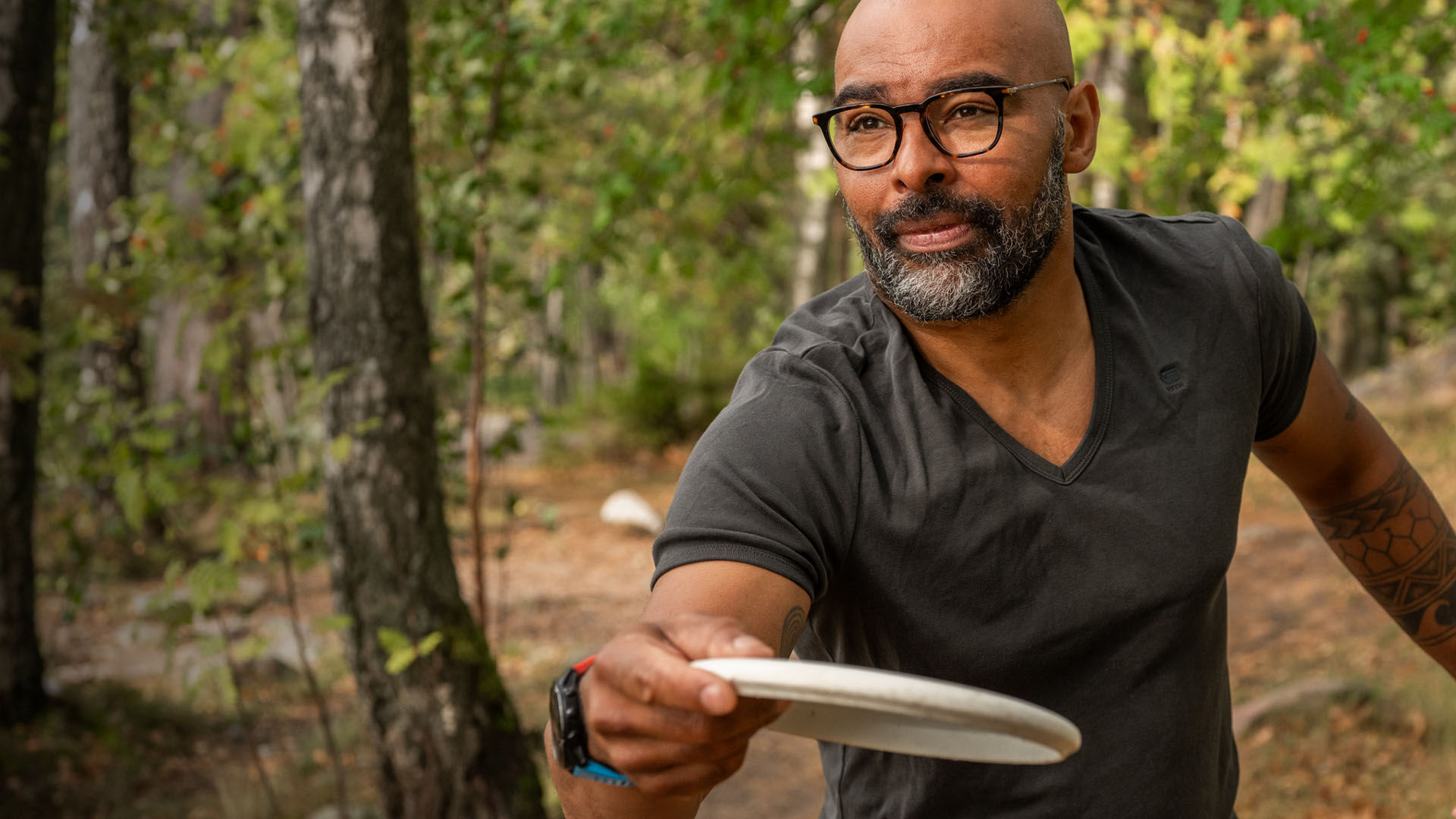 Silmälasipäinen mies frisbeegolf radalla metsässä